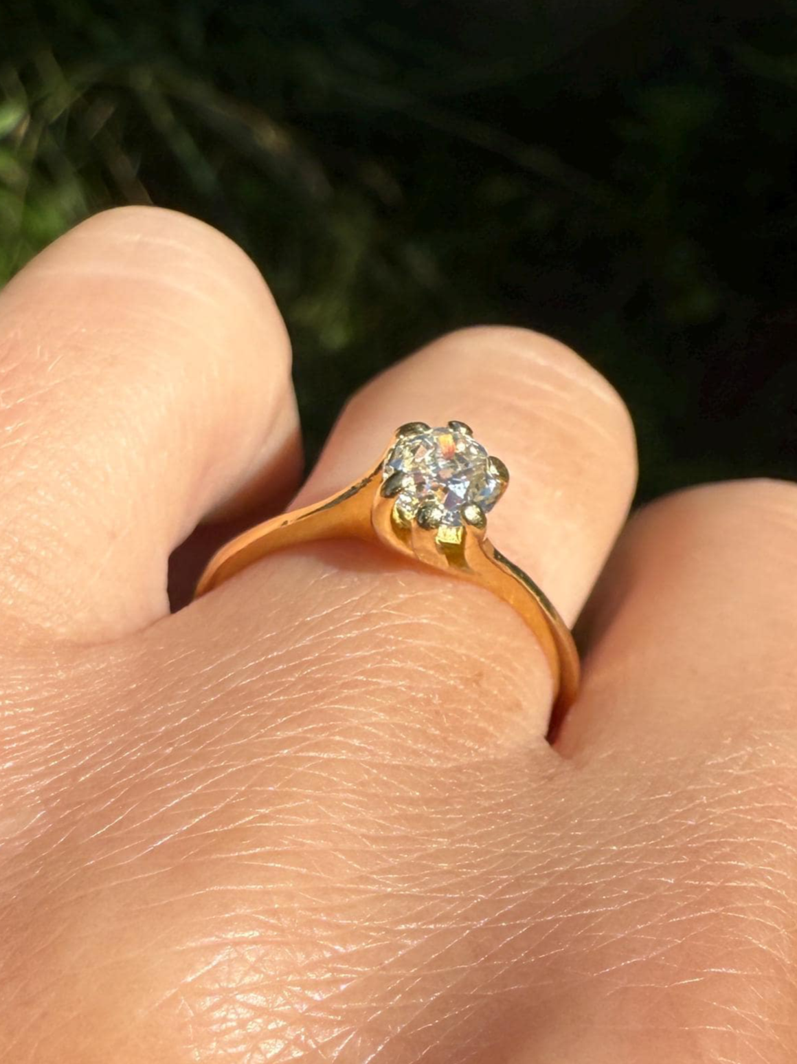 Gold ring with a diamond on a finger against a blurred green background